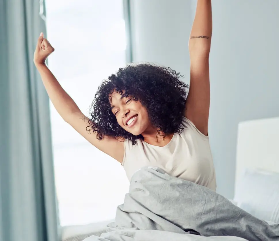 Shot of a happy young woman sitting on the bed in the morning and stretching