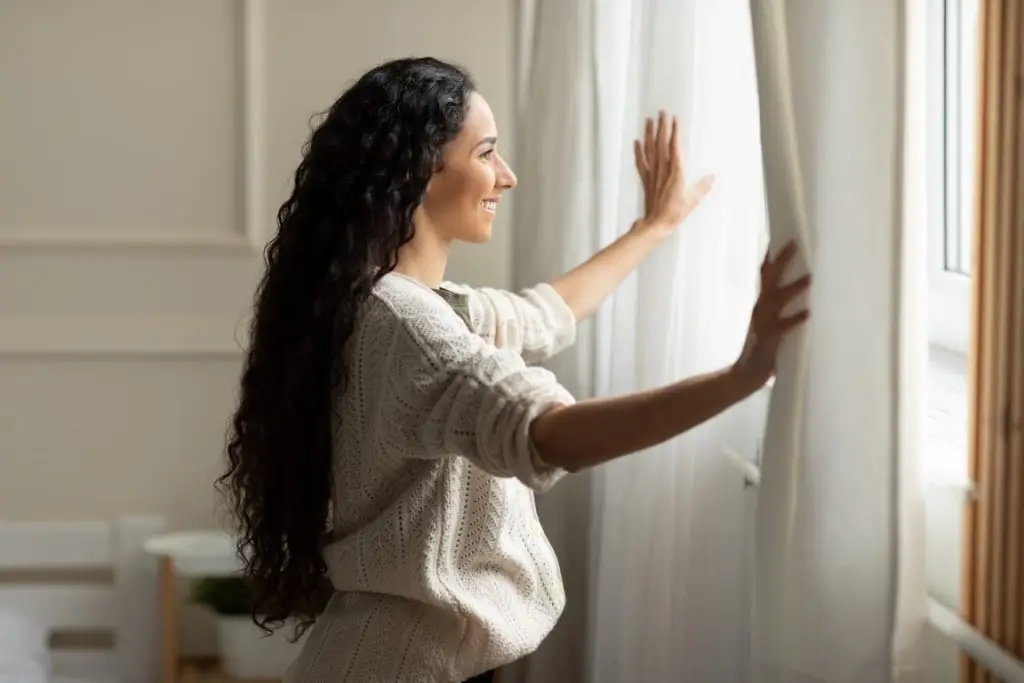 Smiling woman opening window curtains at home stock photo