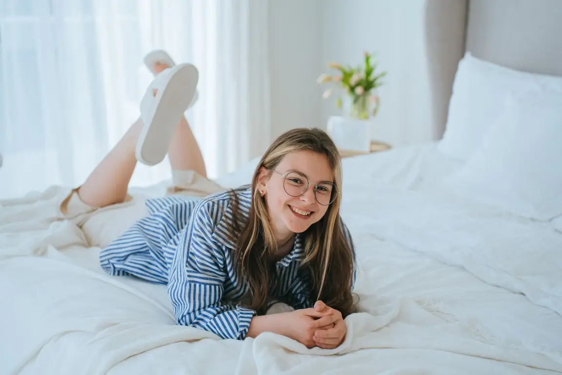 Young girl in casual laying on bed looks at camera smiling broadly enjoying vacations. Cheerful American schoolgirl relaxing at home. Domestic leisure. Teenagers on holidays. stock photo