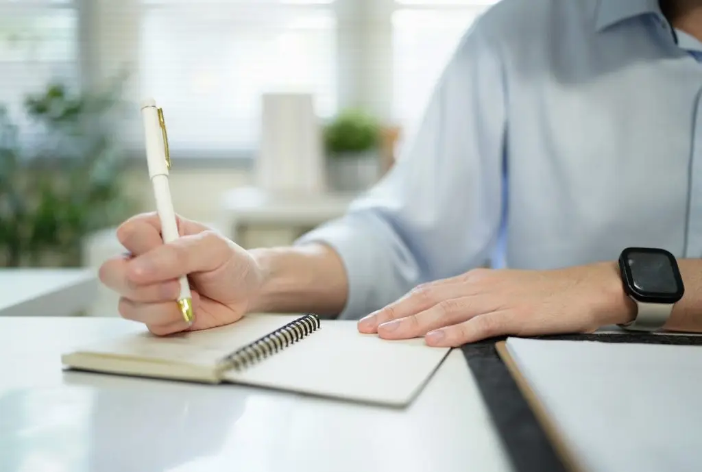 Businessman analyzing data (graphs/charts) on a document, taking notes with a pen. Office setting, professional work stock photo